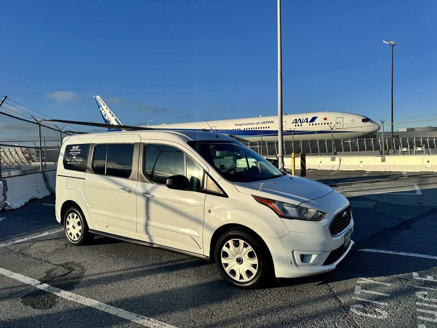 On-Off Transportation white passenger vehicle at an airport with an ANA airplane in the background